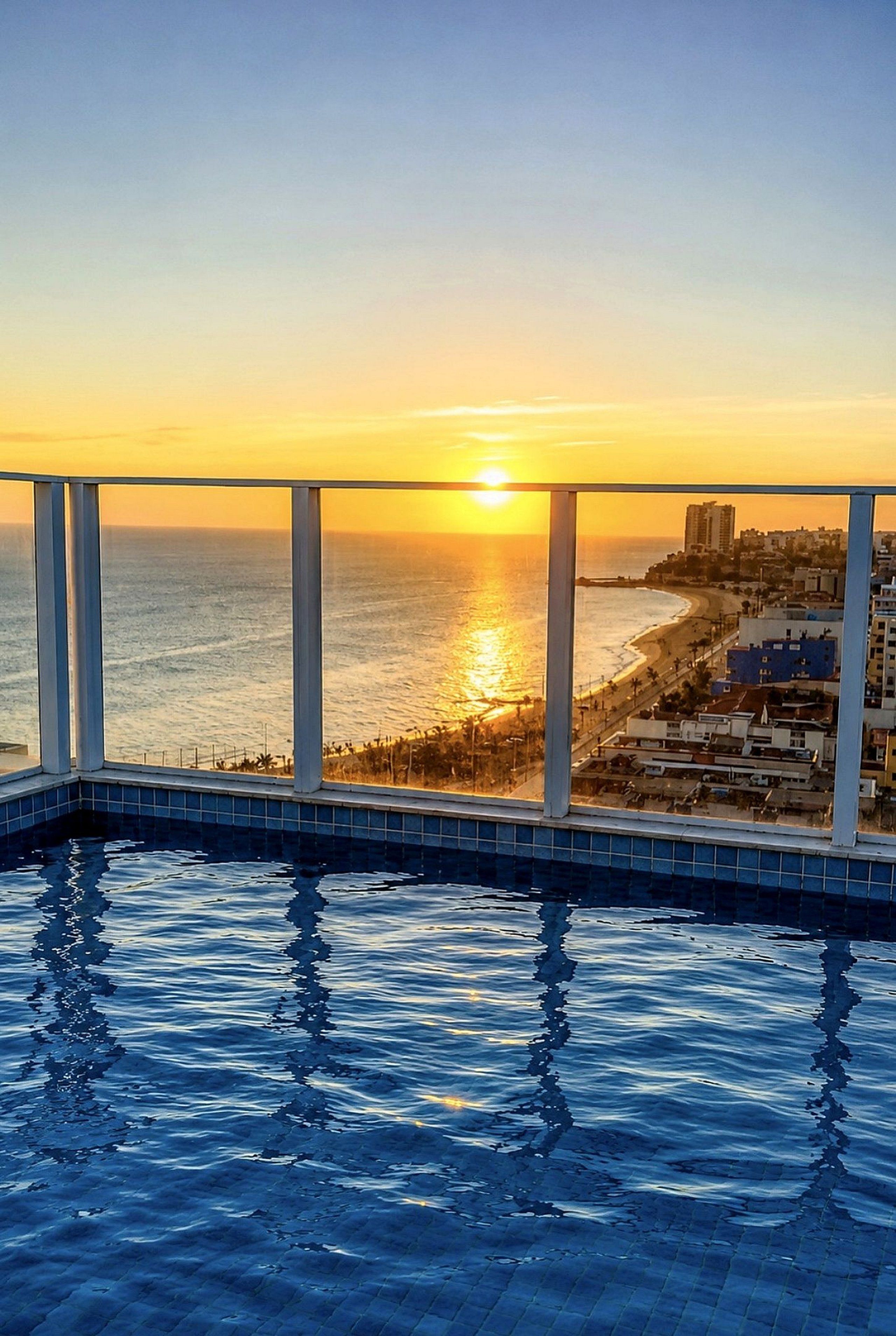 A pool with a view of the ocean and a cityscape at sunset.