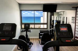 Ein Fitnessraum mit Trainingsgeräten, einem großen Fenster mit Meerblick und motivierenden Wandbildern.