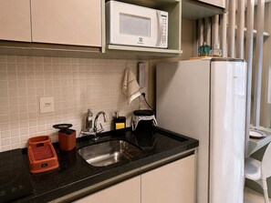 A kitchen with a black countertop, a white microwave, a sink, and a refrigerator. - Costa Azul 403 (Salvador)