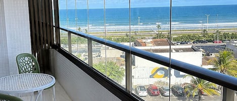 A balcony with a view of the ocean, a table, and two chairs.
