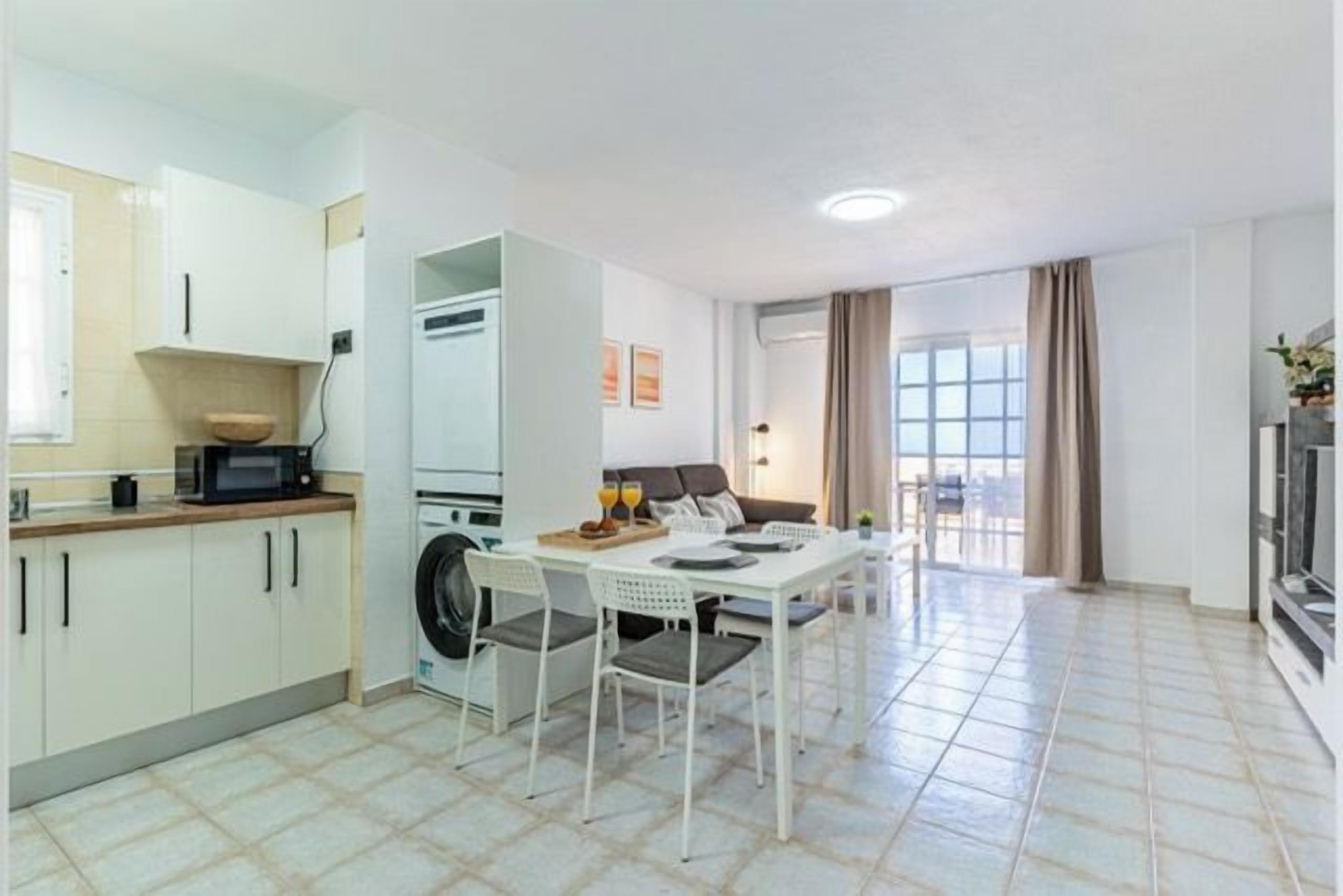 A compact kitchen with a dining area, a washing machine, and a large window.