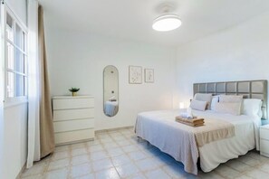 Ein Schlafzimmer mit Bett, Nachttisch, Kommode und einem Fenster mit Vorhängen.