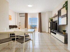 A modern kitchen with a dining area, a flat-screen TV, and a view to the outside. - Apartment with terrace & views in Adeje (Torviscas Alto)