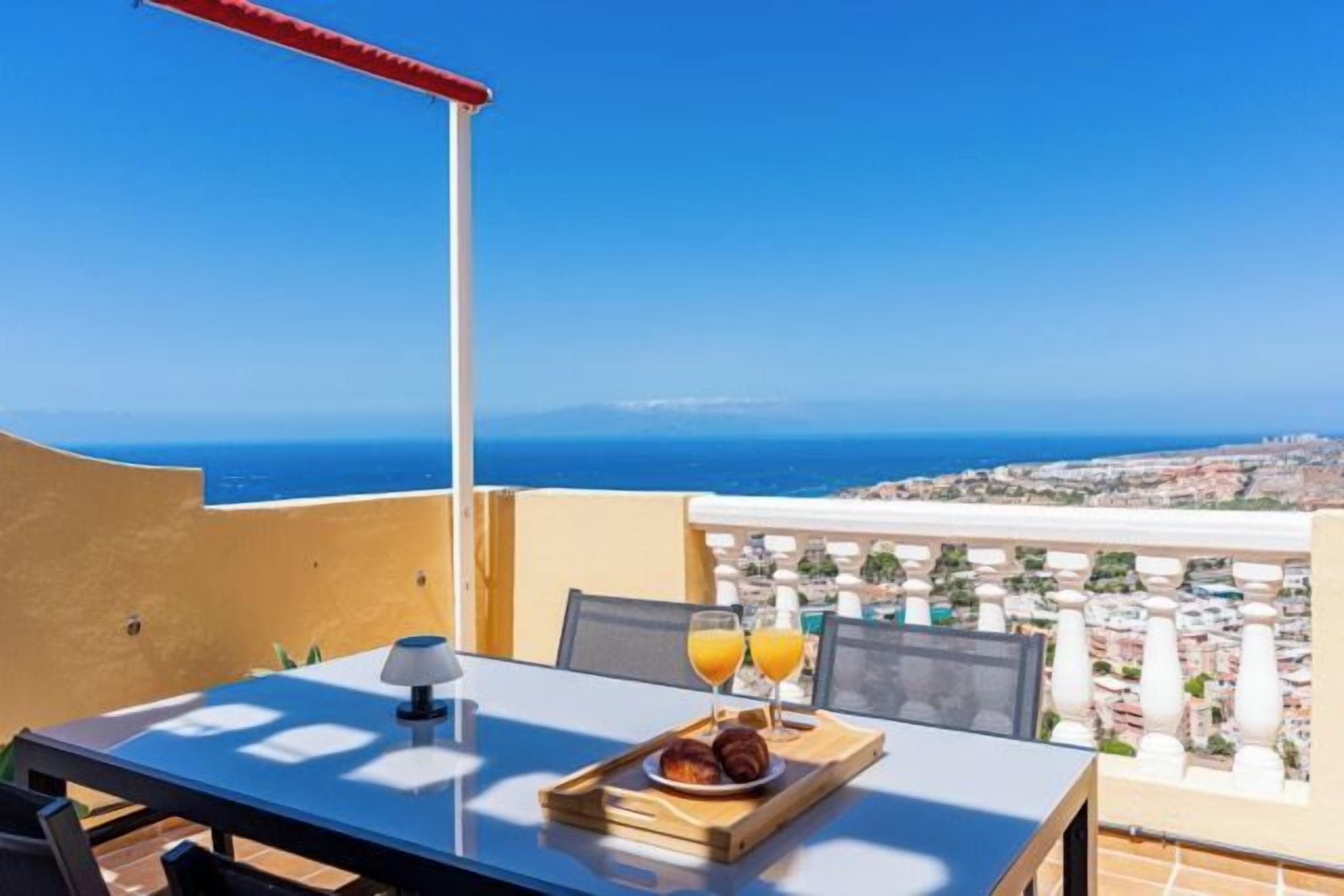 Un balcón con una mesa lista para el desayuno, con vistas a una ciudad costera.