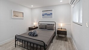 Quarto com cama, duas mesas de cabeceira, ar-condicionado na parede e janela com persianas.