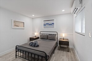 Een slaapkamer met een bed, twee nachtkastjes, een wandairconditioner en een raam met zonwering.
