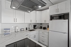 Una cocina moderna con armarios blancos, microondas integrado, refrigerador y cafetera.