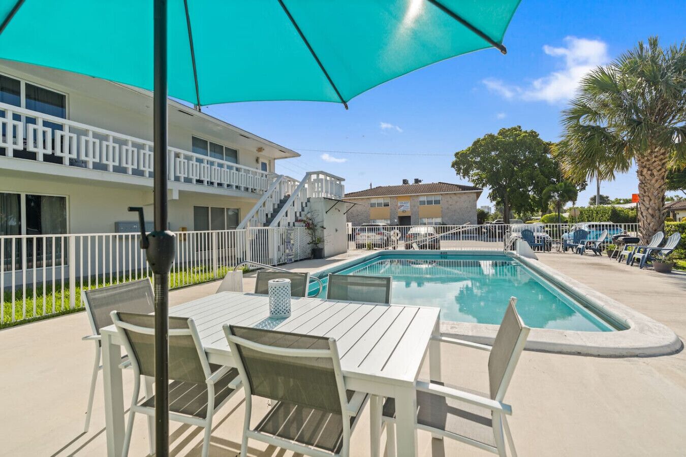 A pool area with a table and chairs, a large umbrella, and a building in the background.