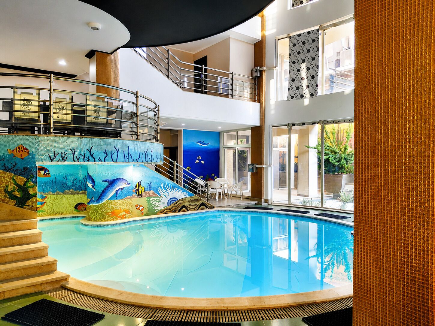 An indoor swimming pool with a dolphin mural, a staircase, and a view of the outdoors.