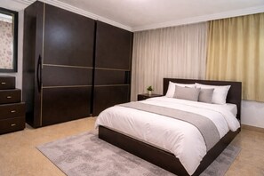 A bedroom with a large bed, dark wardrobe, and a nightstand with a plant. - Family Room in a Luxury Villa (New Cairo)