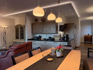 A modern kitchen with a dining area, featuring pendant lights, a wooden dining table, and a sofa. - Erlenhof Vacation Rental - Modern Penthouse in Monschau (Monschau)