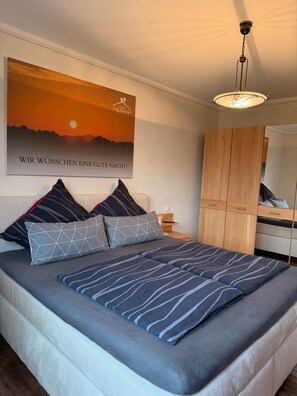 A bedroom with a bed, pillows, a nightstand, a wardrobe, and a wall-mounted poster. - Erlenhof Vacation Rental - Modern Penthouse in Monschau (Monschau)