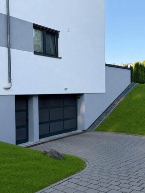 A modern two-story building with a garage door, a paved driveway, and a grassy area. - Erlenhof Vacation Rental - Modern Penthouse in Monschau (Monschau)