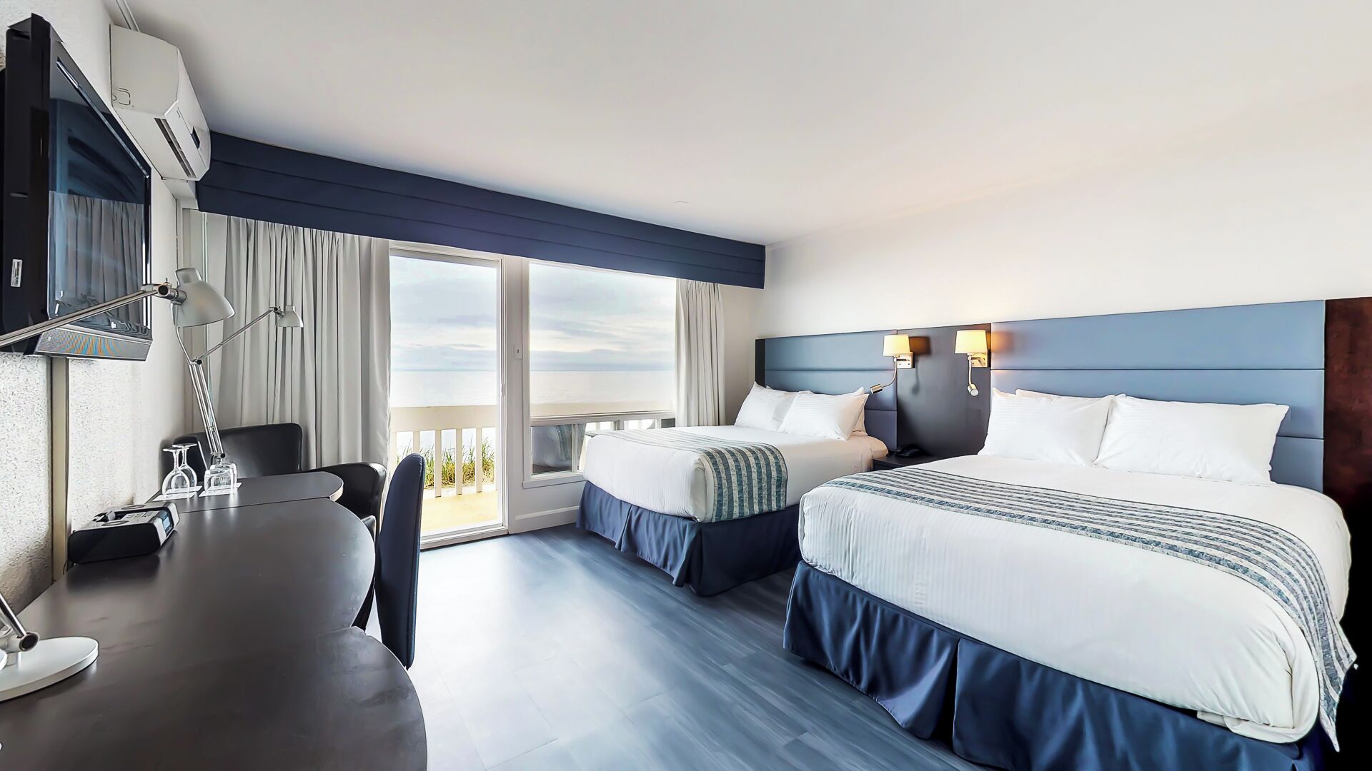 A hotel room with two beds, a desk, a chair, and a large window with a view.