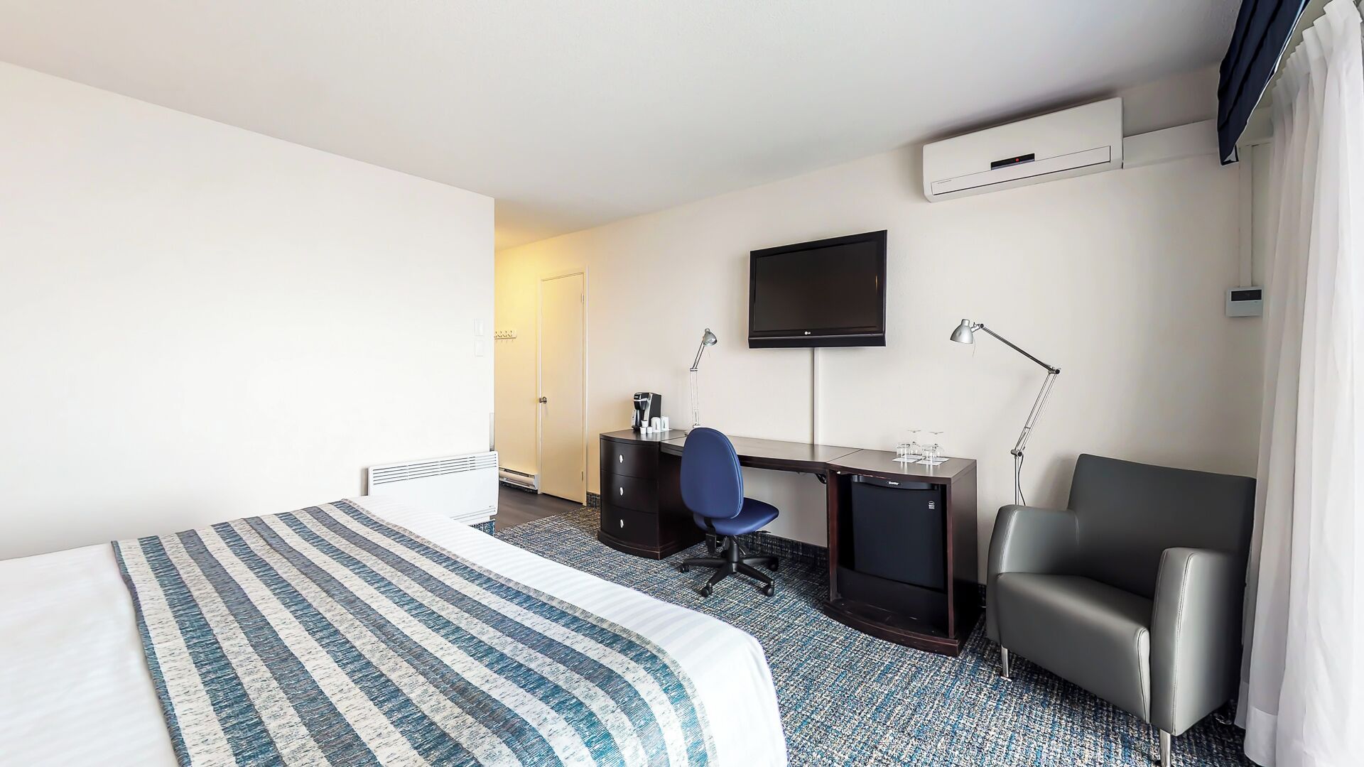 Une chambre d’hôtel équipée d’un lit, d’un bureau, d’une chaise, d’une télévision et d’un appareil de climatisation.