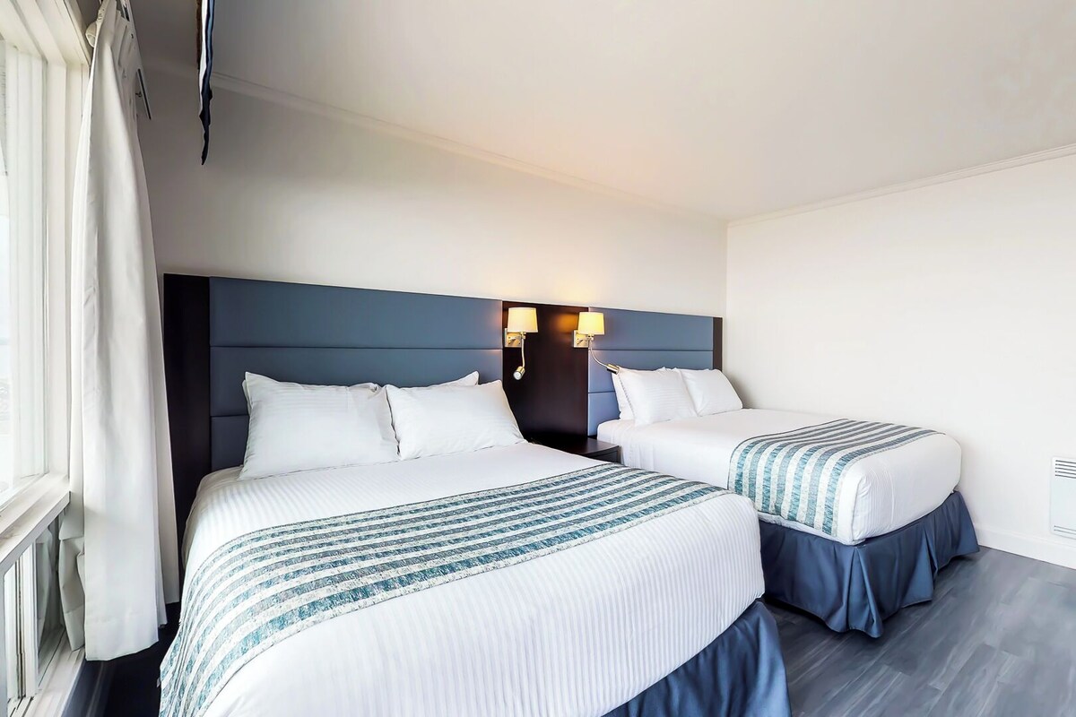 A hotel room with two beds, a dark headboard, bedside lamps, and a window with curtains.
