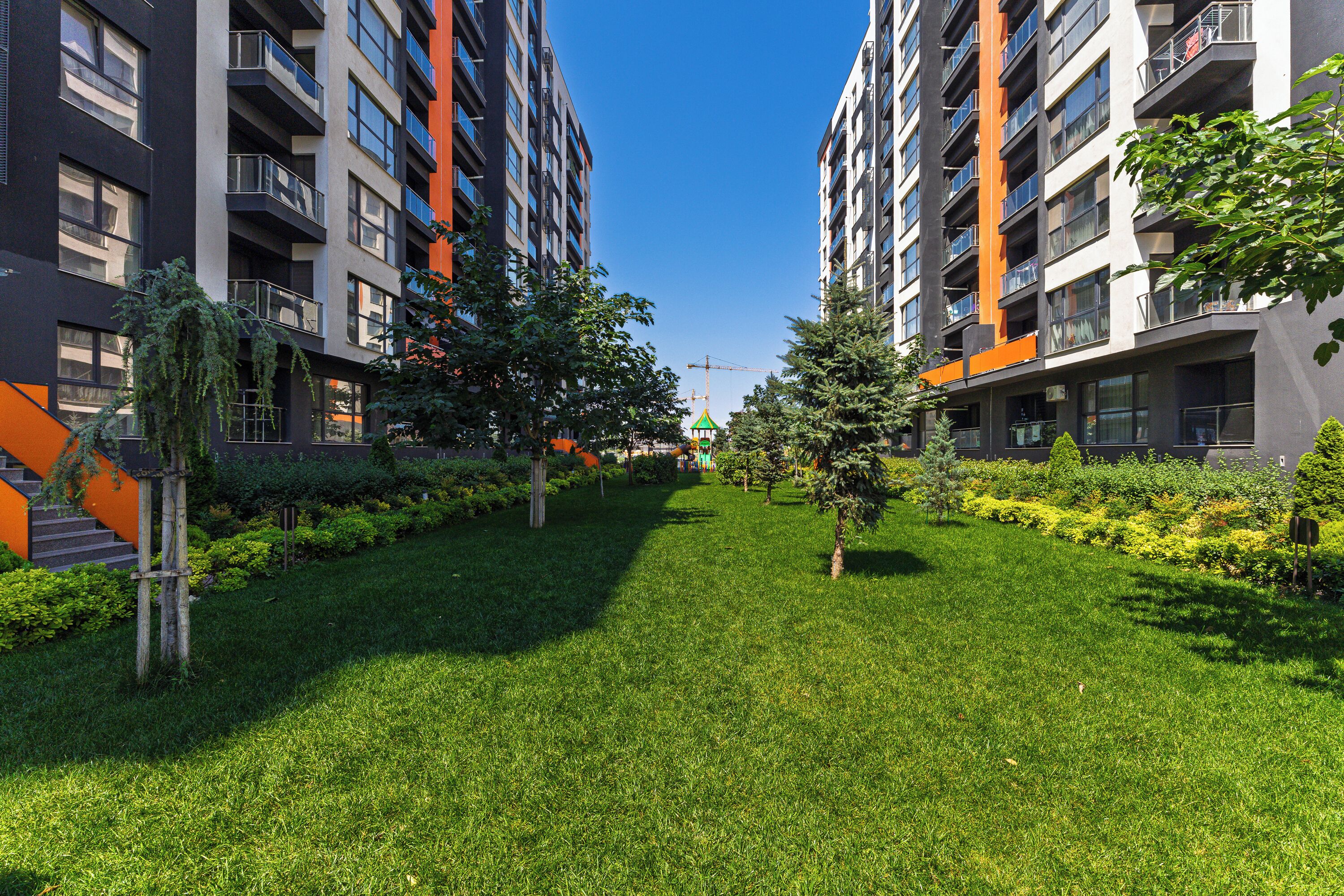A modern apartment complex with multiple floors, balconies, and a well-maintained grassy area with trees.