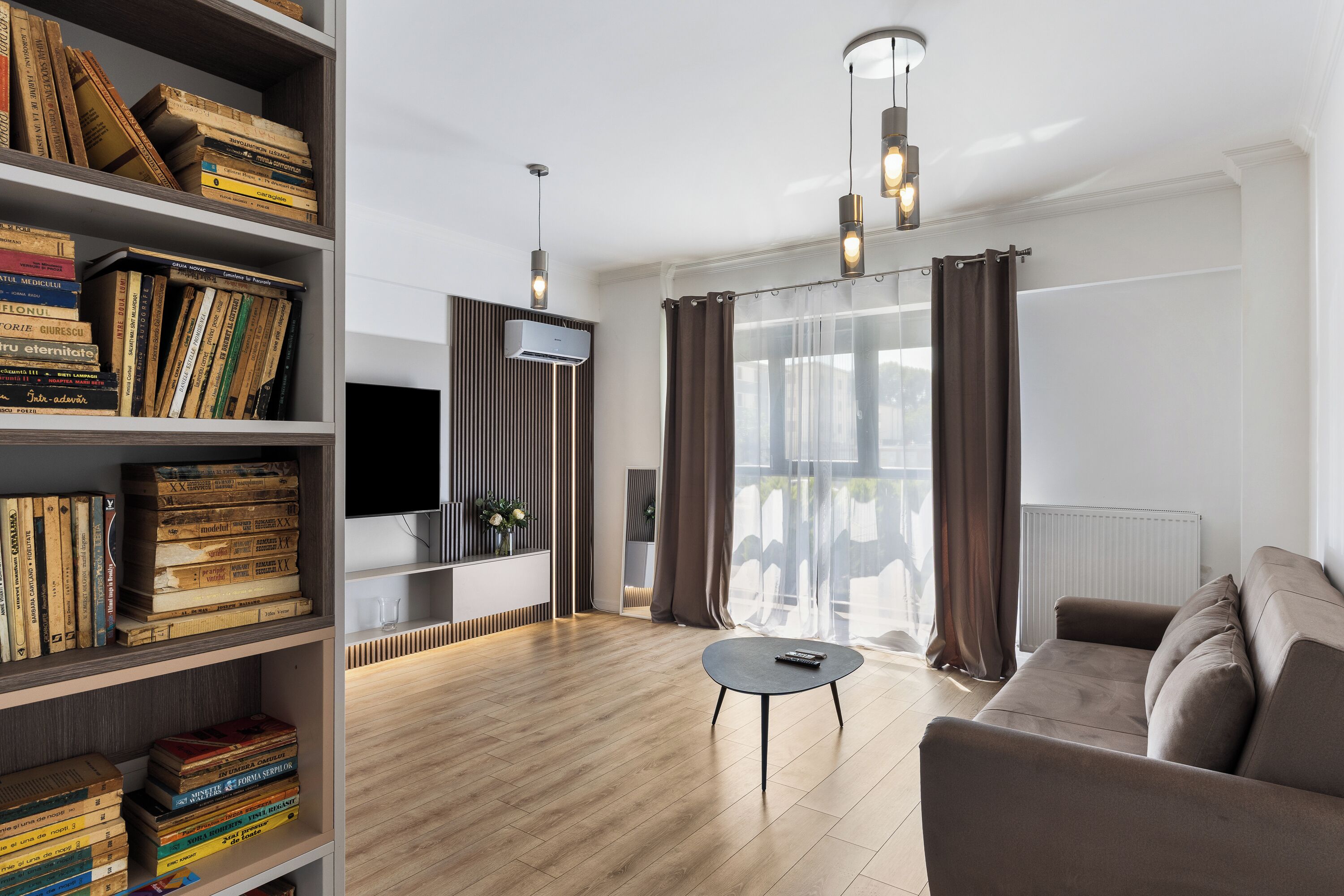 A modern living room with a wooden floor, a sofa, a coffee table, and a bookshelf filled with books.