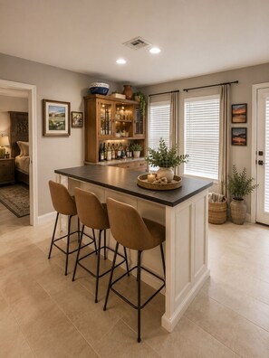 A kitchen with a bar area, featuring a countertop, bar stools, and a cabinet with glassware. - Bayfront 3/2/Loft with pool on Copano Bay with pier (Rockport)
