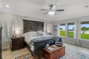 A bedroom with a large bed, a ceiling fan, a nightstand, a wooden chest of drawers, and a view of the outdoors. - Bayfront 3/2/Loft with pool on Copano Bay with pier (Rockport)