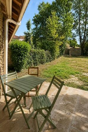 Un patio exterior con una mesa y sillas, rodeado por un muro de piedra y follaje.