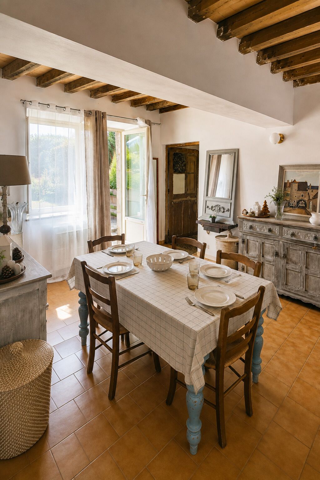 A dining area with a table set for four, wooden chairs, a buffet counter, and a large window with curtains.