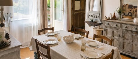 A dining area with a table set for four, wooden chairs, a buffet counter, and a large window with curtains.