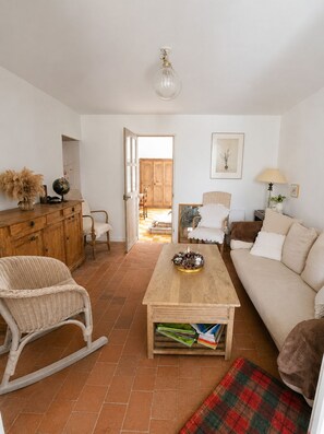Una sala de estar con una mesa de centro de madera, una mecedora de mimbre, un sofá y una puerta que da a un balcón.