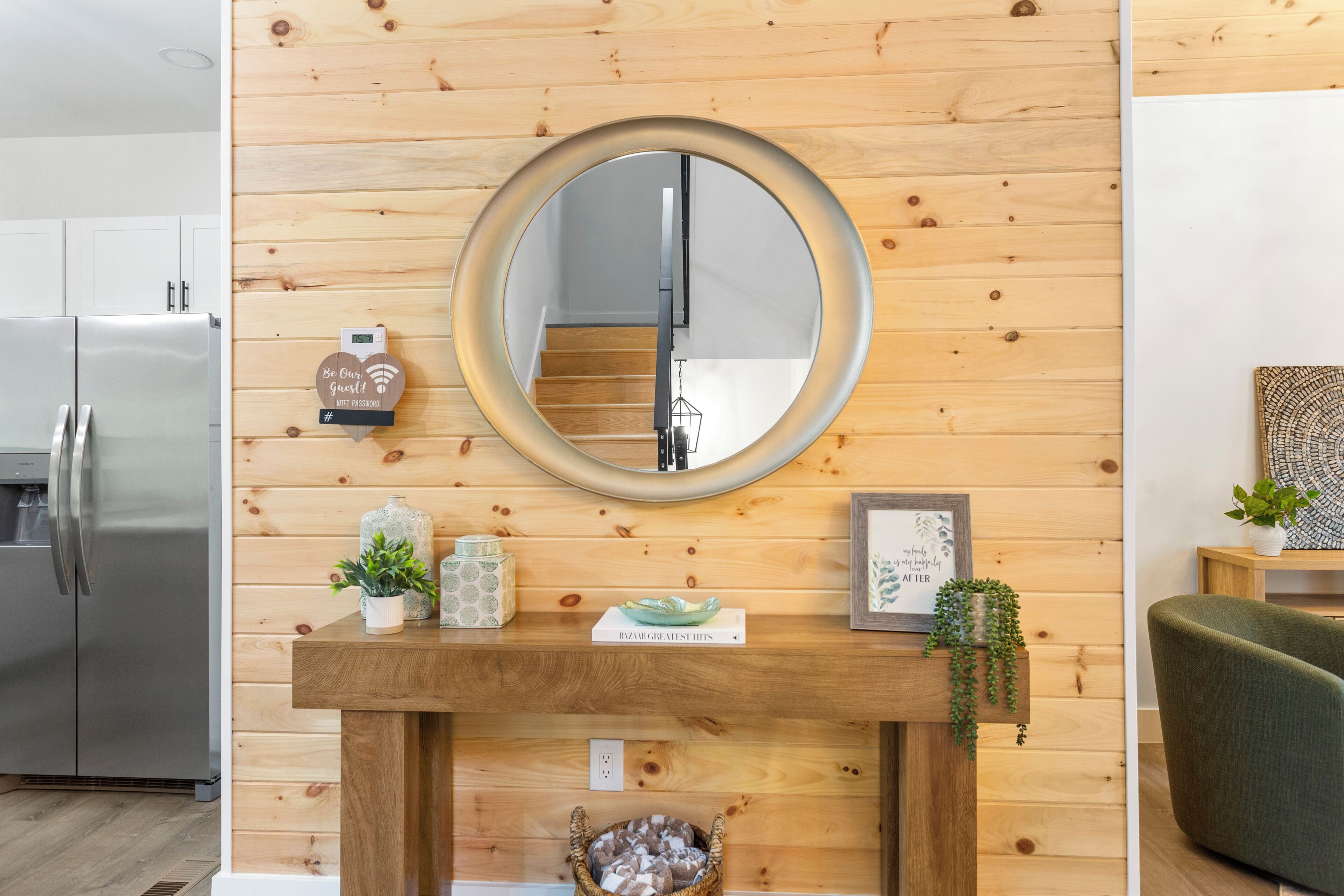 A modern kitchen with a wooden wall, a round mirror, and a small table with decorative items.