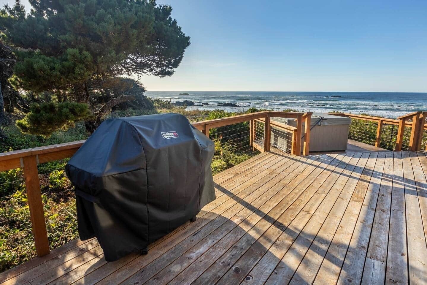 Eine Holzterrasse mit Grill, mit Blick auf einen Strand und den Ozean.