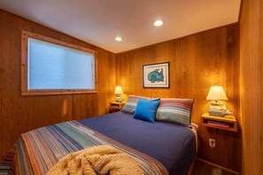 A room with a bed, two bedside lamps, a window with blinds, and a framed picture on the wall. - Solitude in Seal Rock (Seal Rock)