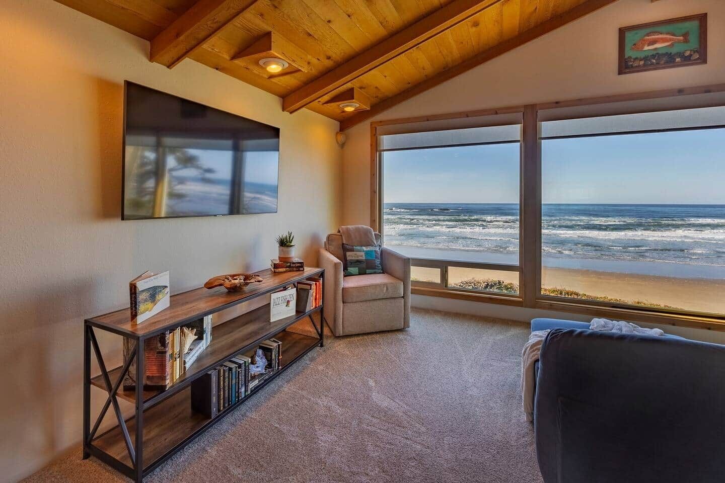Quarto com uma grande janela com vista para o oceano, uma área de estar confortável e uma estante de livros.