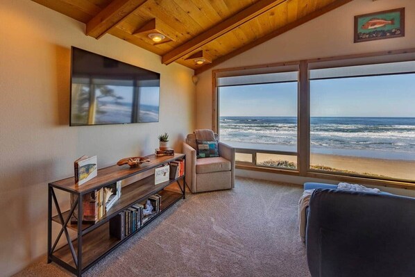 A room with a large window overlooking the ocean, a comfortable seating area, and a bookshelf. - Solitude in Seal Rock (Seal Rock)