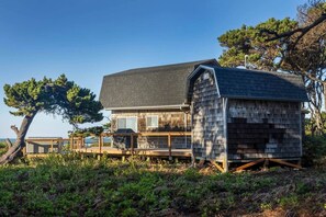 A wooden cabin with a deck, surrounded by trees and vegetation. - Solitude in Seal Rock (Seal Rock)