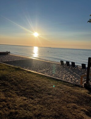 A beach with a sunlit sky, a concrete walkway, and several chairs. - Waterfront Escape - Bay View Beach House (Tawas City)