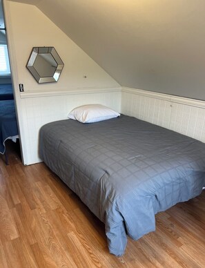 Ein Schlafzimmer mit einem Einzelbett, einem weißen Kissen, einem sechseckigen Spiegel an der Wand und Holzboden.