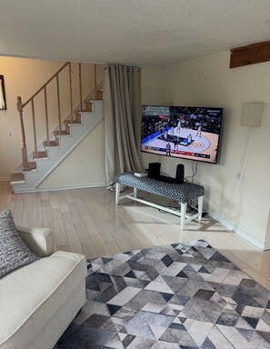 Ein Wohnzimmer mit Fernseher, einer Bank, einer Treppe und einem gemusterten Teppich.