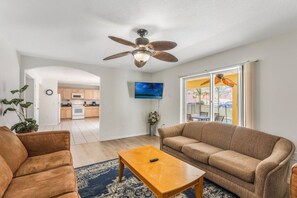 A living room with a sofa, a coffee table, and a ceiling fan. There is a kitchen in the background. - 5 Bedrooms Vacation Home near Disney (Davenport)
