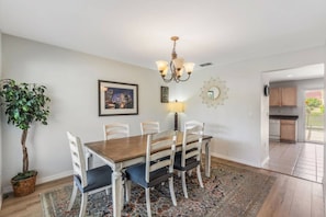 A dining area with a wooden table, white chairs, a chandelier, a potted plant, and a cityscape picture on the wall. - 5 Bedrooms Vacation Home near Disney (Davenport)