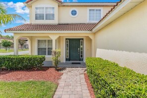 A two-story house with a tiled roof, a green door, and a paved driveway. - 5 Bedrooms Vacation Home near Disney (Davenport)