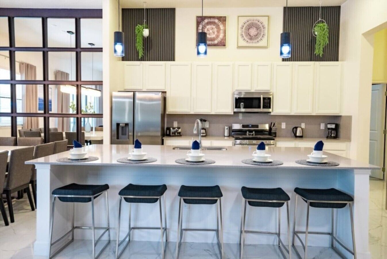 Una cocina moderna con una isla central, taburetes de bar, electrodomésticos de acero inoxidable y decoración en la pared.