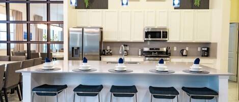 Una cocina moderna con una isla central, taburetes de bar, electrodomésticos de acero inoxidable y decoración en la pared.