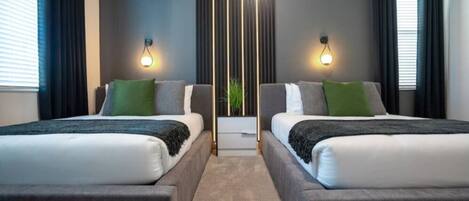 A modern hotel room with two beds, a central light fixture, and a view of the outdoors.