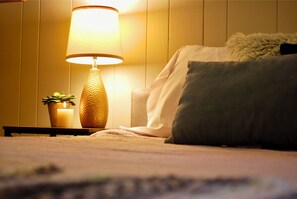 A bed with a pillow, a bedside table with a lamp, and a small plant.