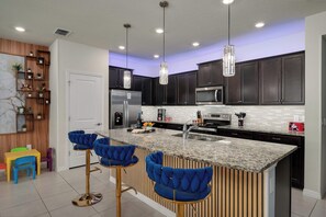 A modern kitchen with dark cabinets, stainless steel appliances, and a marble countertop. - Themed 5BR Near Disney - Private Heated Pool & Mario Arcade (Davenport)