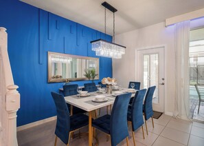 A dining area with a blue accent wall, a chandelier, a mirror, and a table set for four. - Themed 5BR Near Disney - Private Heated Pool & Mario Arcade (Davenport)