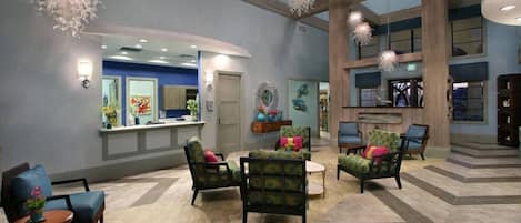 A spacious lobby with a reception desk, multiple seating areas, and a high ceiling with hanging light fixtures.
