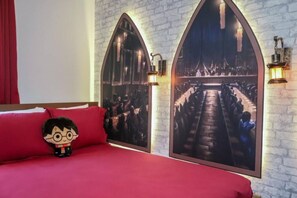 Une chambre avec un lit rouge, un jouet en peluche et deux grandes images encadrées accrochées au mur.