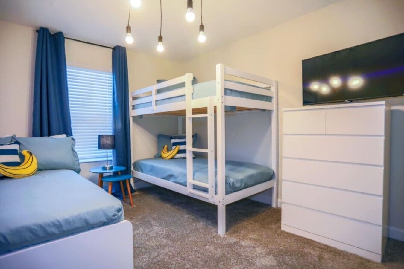 A bunk bed room with a desk and chair, a TV, and a window with curtains.
