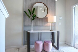 Un interno moderno con una consolle, uno specchio tondo, una lampada e due pouf rosa.